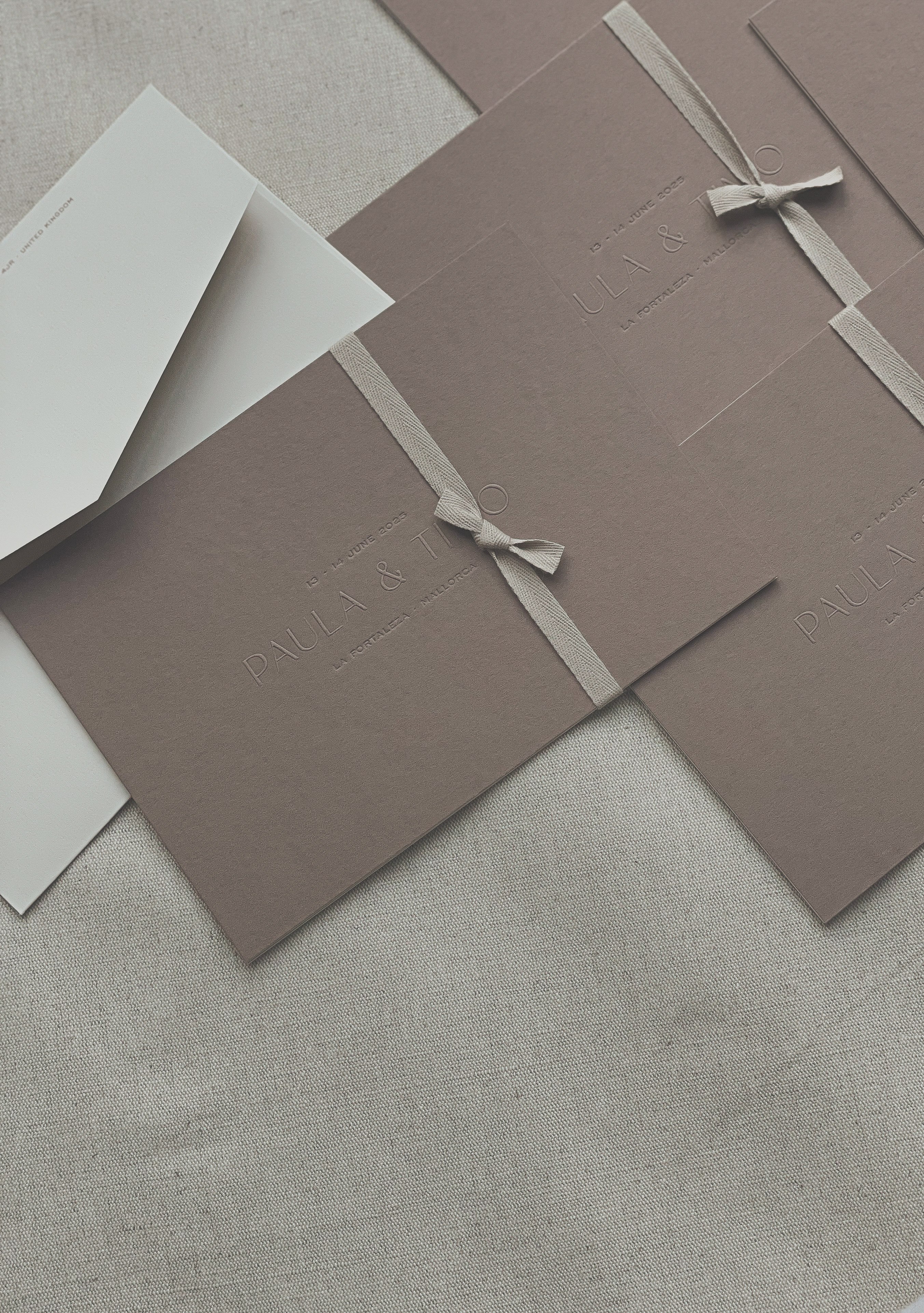 Geprägte Hochzeitseinladungen auf mokkafarbenem Papier mit Baumwollband für eine Destination Wedding auf Mallorca, gestaltet von Wedding Mark