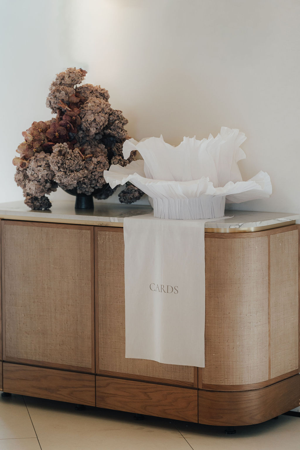 Kartenbox mit gerüschtem Seidenpapier auf einem Rattan-Sideboard mit Trockenblumen — Schild für Karten aus Baumwolle